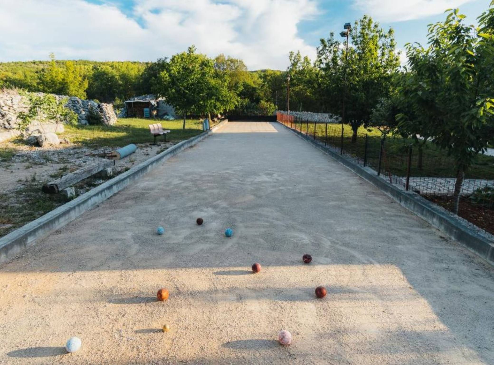 Un terrain de croquet entouré d’une clôture en filet, avec des arbres et un ciel dégagé.