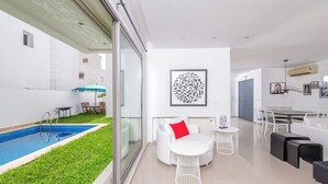Ein modernes Wohnzimmer mit Pool, weißen Möbeln und einem Essbereich.