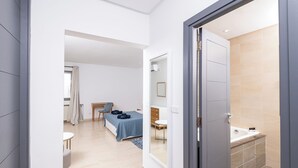 Ein modernes Hotelzimmer mit Bett, Schreibtisch, Stuhl, kleinem Tisch und einem Badezimmer mit Waschbecken und Dusche.