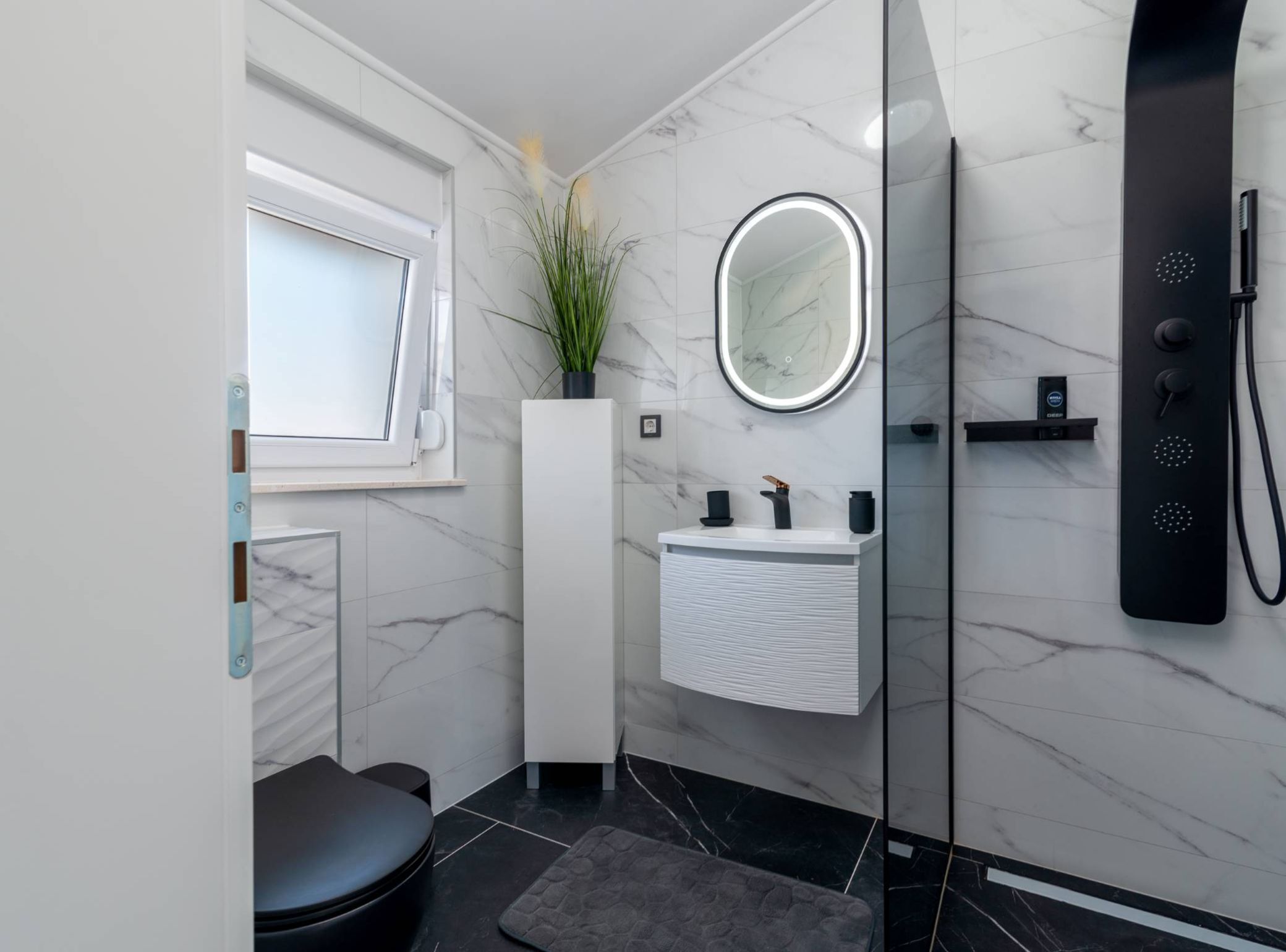 Een moderne badkamer met een wit wastafelmeubel, een ronde spiegel, een douche met handdouche en een potplant.
