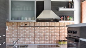 Une cuisine moderne avec des meubles de couleur sombre, un pare-feu en carreaux, un évier en acier inoxydable et une hotte aspirante.