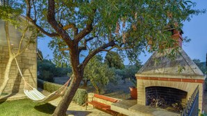 Une terrasse en pierre avec une cheminée en briques, un hamac et un banc.