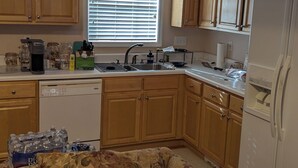 A compact kitchen with wooden cabinets, a built-in dishwasher, a refrigerator, and a window with blinds. -  1-bdrm house with fireplace, AC and WiFi with 20 acres of  trees scenic deck. (Kingston)