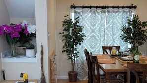 A dining area with a wooden table and chairs, a potted plant, and a window with patterned curtains. -  1-bdrm house with fireplace, AC and WiFi with 20 acres of  trees scenic deck. (Kingston)