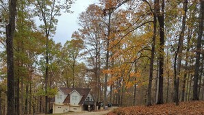 A house with a gravel driveway leading to a wooden deck, surrounded by trees with autumn foliage. -  1-bdrm house with fireplace, AC and WiFi with 20 acres of  trees scenic deck. (Kingston)