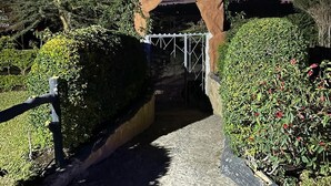 A pathway leading through a garden with a decorative archway and a metal gate.