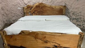 A wooden bed with a natural finish, set against a textured wall.