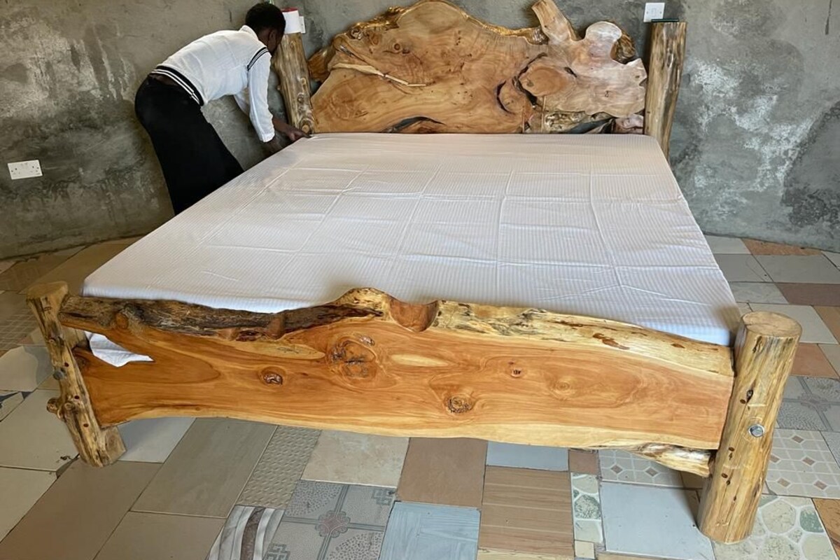 A bed with a unique wooden frame and a white mattress in a room with a concrete wall and patterned floor tiles.