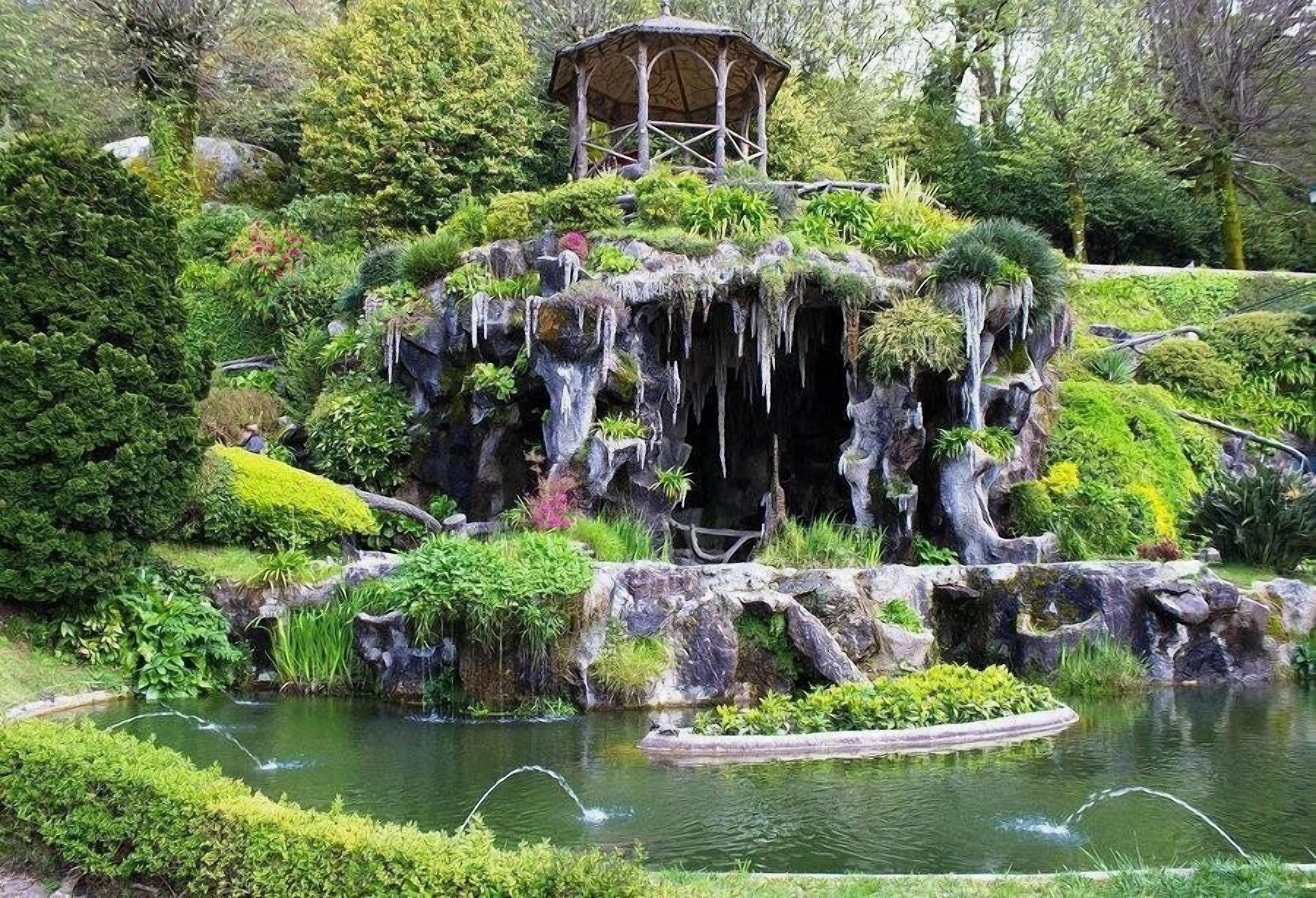Jardim rochoso com um pequeno lago, um gazebo e vegetação exuberante.