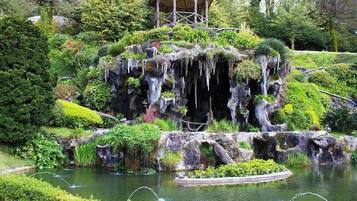 Jardim rochoso com um pequeno lago, um gazebo e vegetação exuberante.
