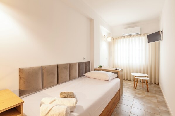 Una habitación de hotel con cama, una mesita, un televisor en la pared y una ventana con cortinas.