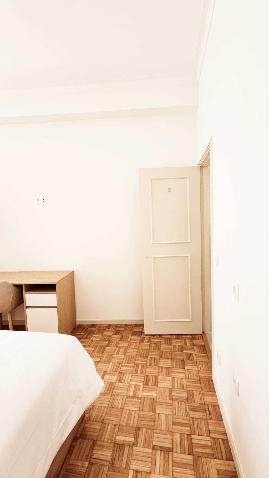 A bedroom with a bed, a desk, and a wardrobe.