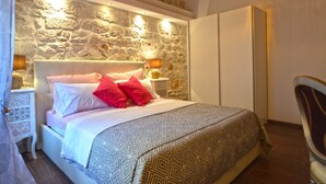 A bedroom with a stone wall, a bed with patterned bedding, bedside lamps, and a wardrobe. - Elegant Rovinj Old Town Apartment (Rovinj)