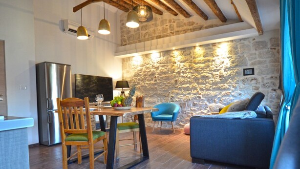 A cozy living area with a stone wall, wooden furniture, and a modern kitchen. - Elegant Rovinj Old Town Apartment (Rovinj)