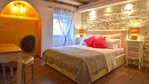 A bedroom with a stone wall, a bed with patterned bedding, a chair, and a desk. - Elegant Rovinj Old Town Apartment (Rovinj)