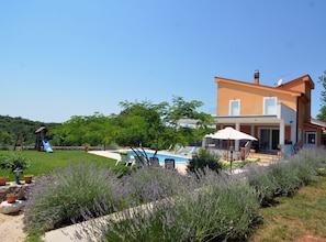 Ein zweistöckiges Haus mit Swimmingpool, Sitzgelegenheit im Freien und einem Garten mit Lavendelpflanzen.