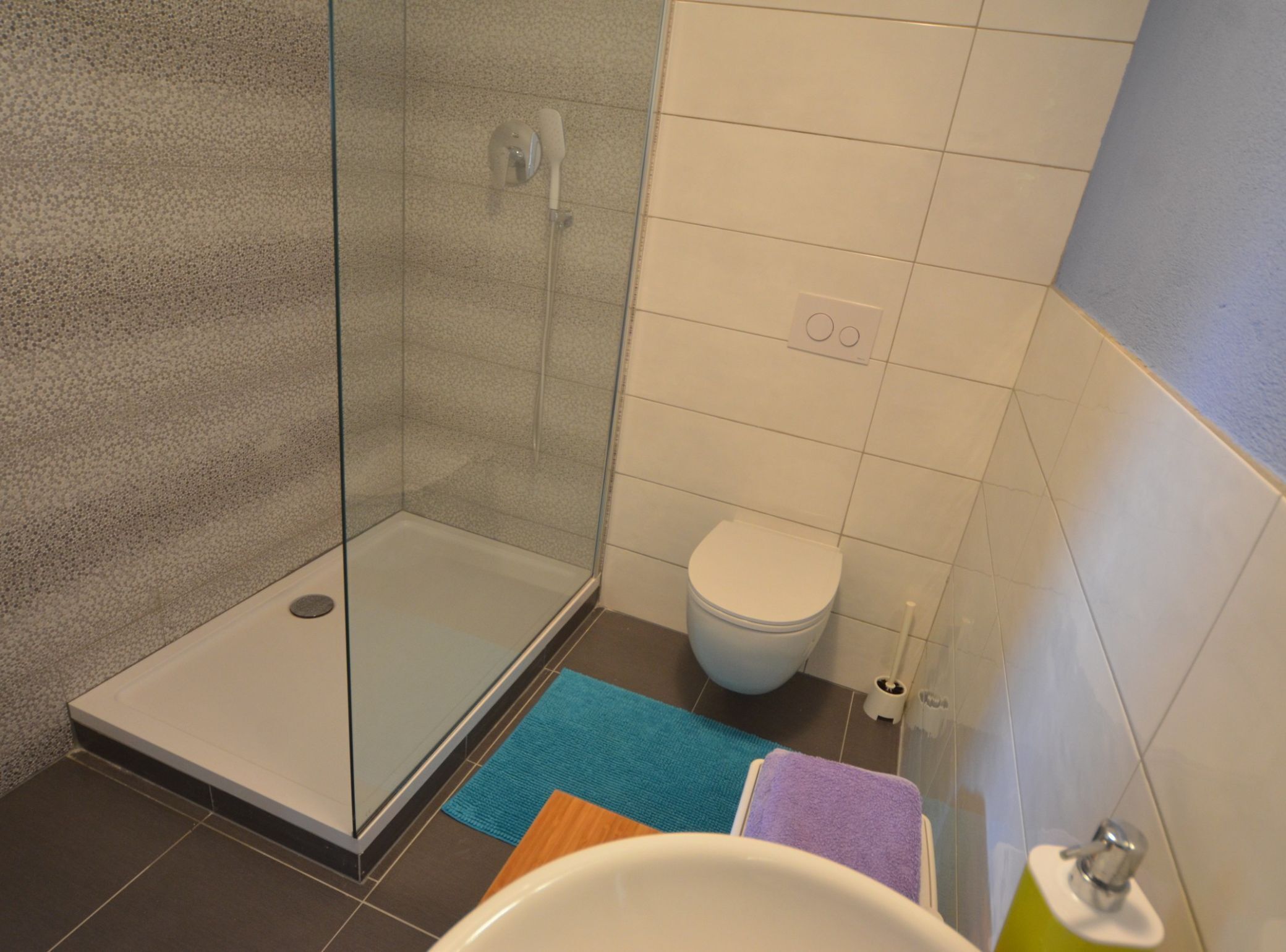A bathroom with a glass shower enclosure, a toilet, and a sink with a towel.