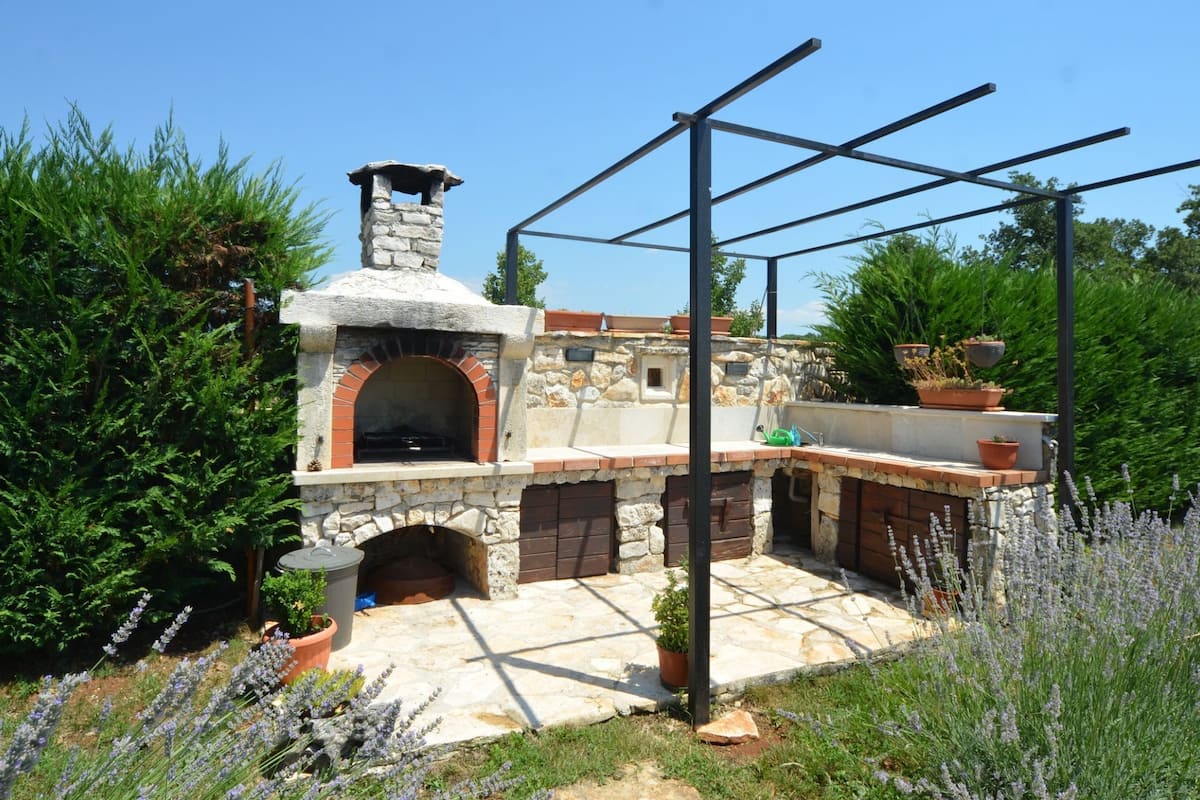 A stone-built outdoor kitchen with a brick oven, surrounded by potted plants and lavender.
