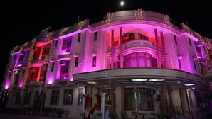 Um hotel com vários andares e fachada curva, iluminado por luzes rosa e vermelhas, com uma entrada visível e uma escadaria.