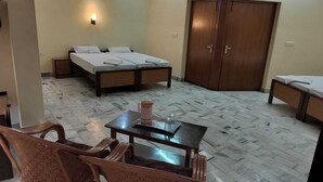 Quarto de hotel com duas camas, um guarda-roupa de madeira, uma mesa pequena com um jarro e copos, e uma cadeira.