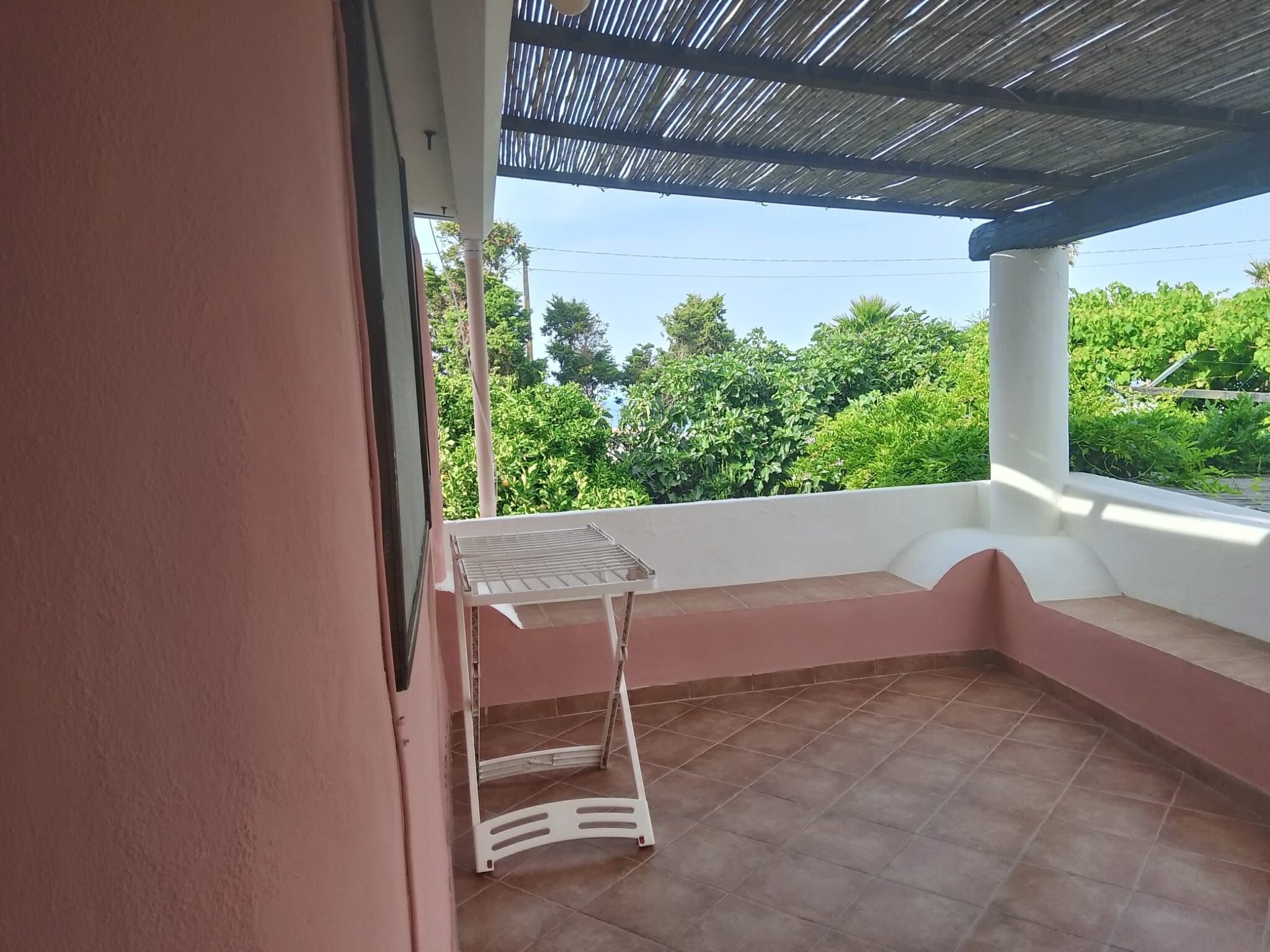 A balcony with a metal table and a white chair, surrounded by a pink wall and a tiled floor.