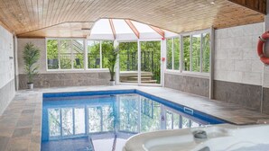 Piscina com hidromassagem, teto de madeira e amplas janelas com vista para o verde.