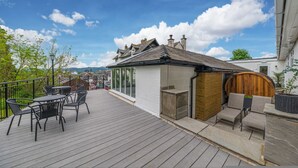 Um deck de madeira com área de estar ao ar livre, estrutura de vidro e vista dos arredores.