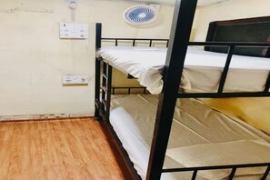 Habitación con literas, suelo de madera, ventilador de pared y enchufes.