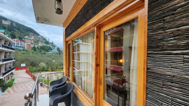 A balcony with a wooden railing, a lantern, and a view of a hillside with buildings. - Di Villa (Manali)
