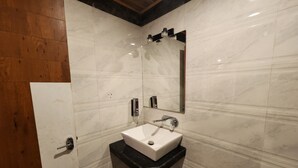 A modern bathroom with a white sink, black countertop, and marble walls. - Di Villa (Manali)