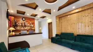 A reception area with a wooden wall, a reception desk, a green sofa, and a blue tufted headboard. - Di Villa (Manali)