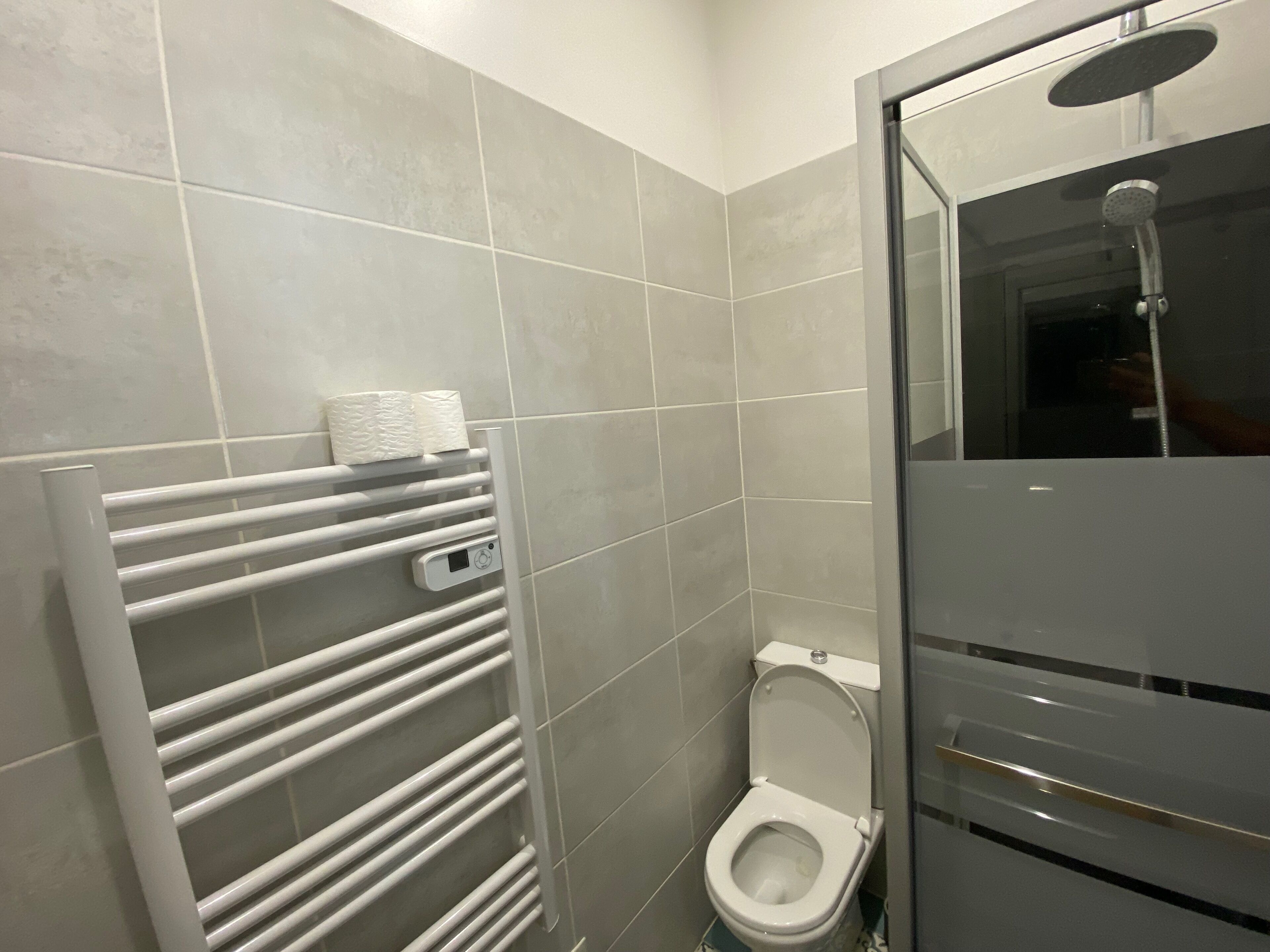 Een moderne badkamer met toilet, douche en een handdoekrek met bedieningspaneel.