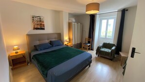 A bedroom with a large bed, bedside tables, a chair, and a window with curtains. - Le repos des Thermes (Rochefort)