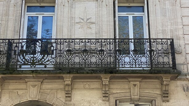 A historic building with ornate architectural details, including a balcony with decorative ironwork and a large arched doorway. - Le repos des Thermes (Rochefort)