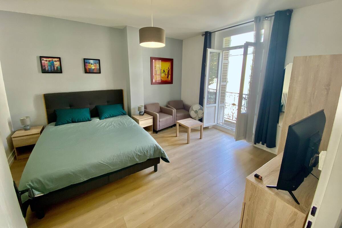 A bedroom with a bed, bedside tables, a desk, a chair, a TV, and a balcony with a view.
