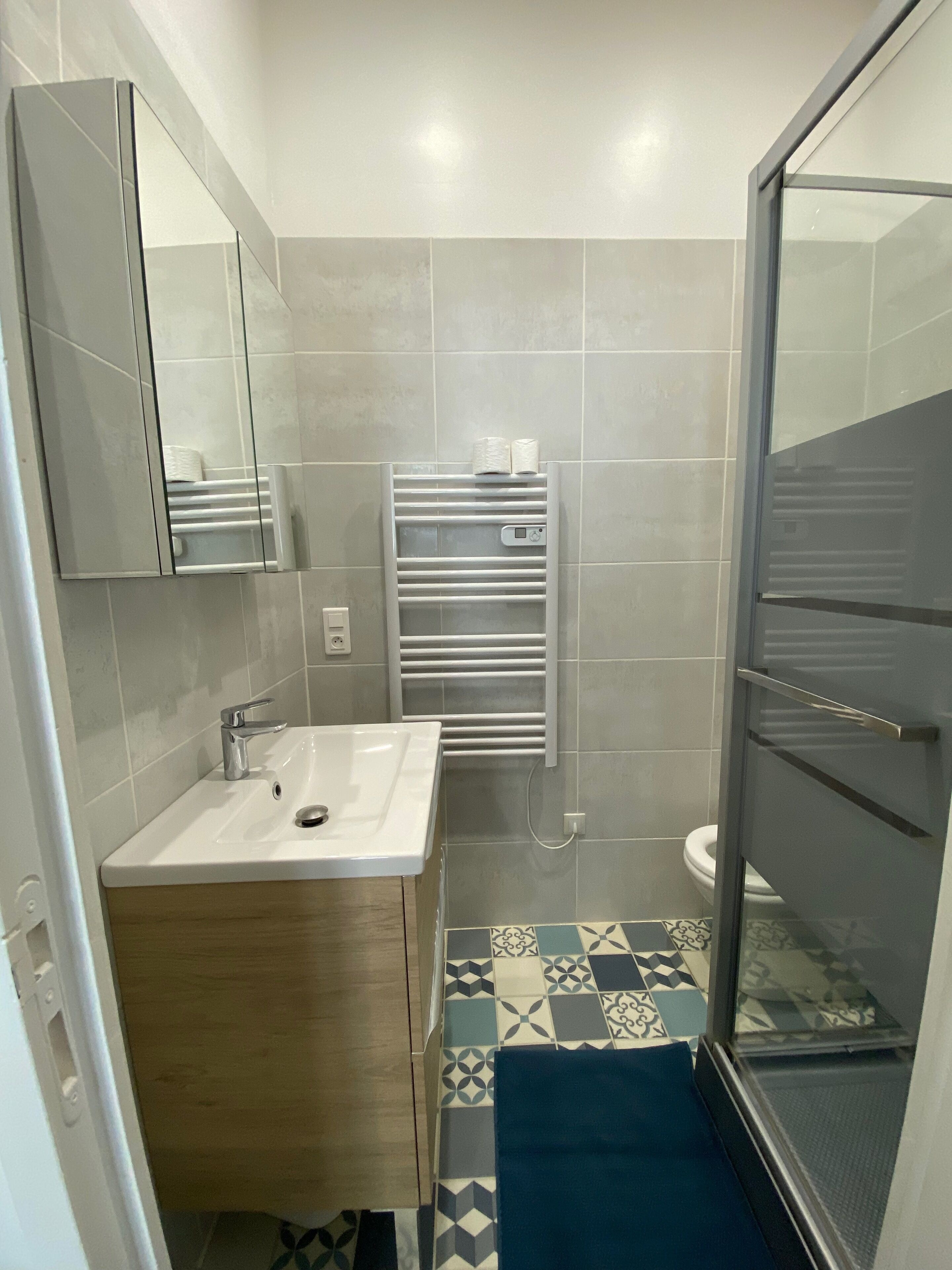 Un baño moderno con un lavamanos blanco, un espejo, un perchero y una zona de ducha.