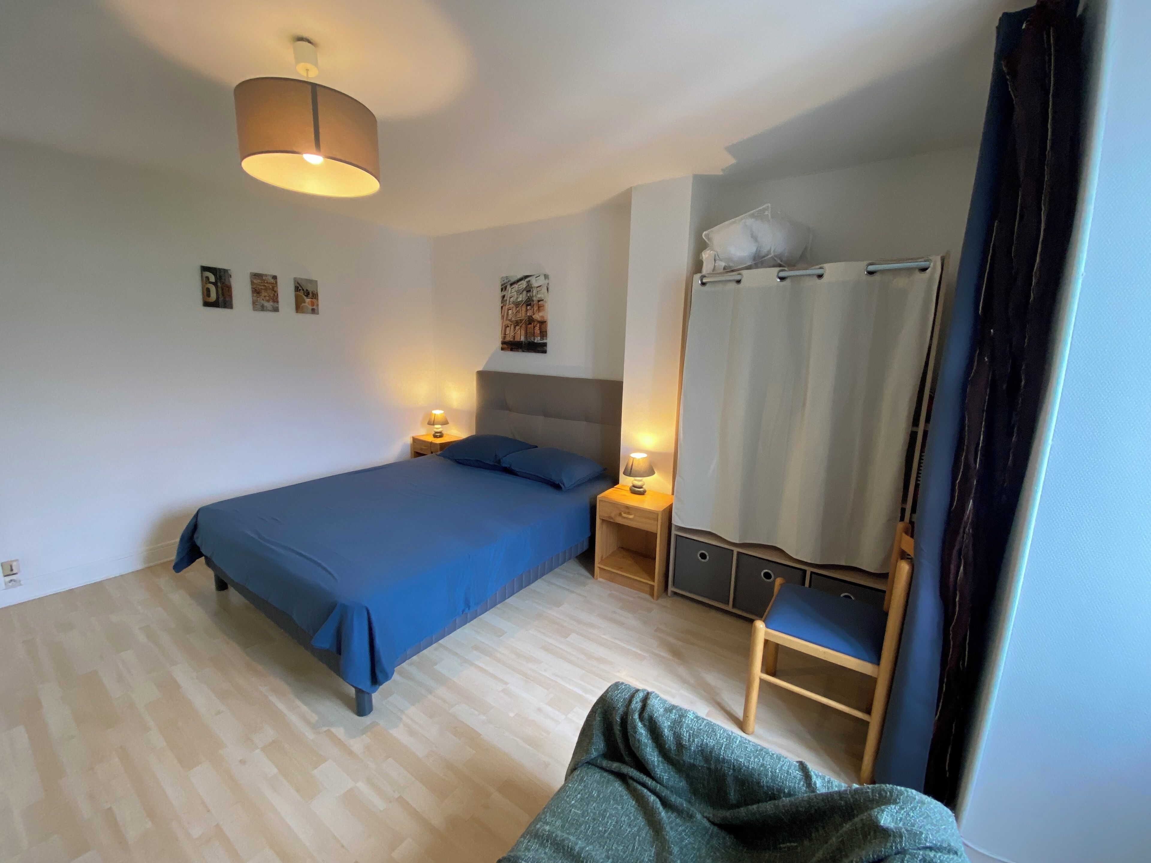 Un dormitorio con cama, lámparas de noche, una silla y una cortina.