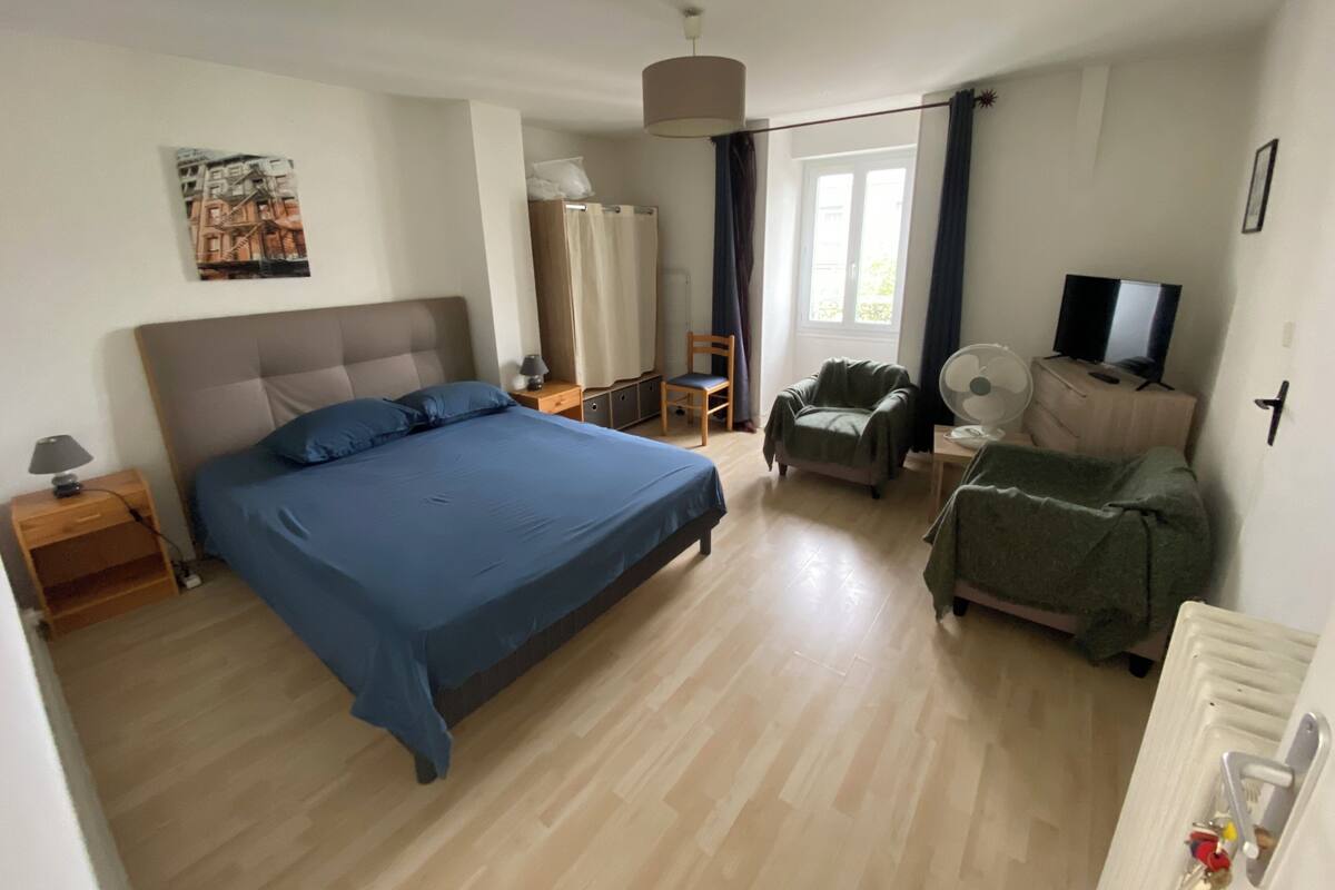 A bedroom with a large bed, a chair, a TV, and a desk.