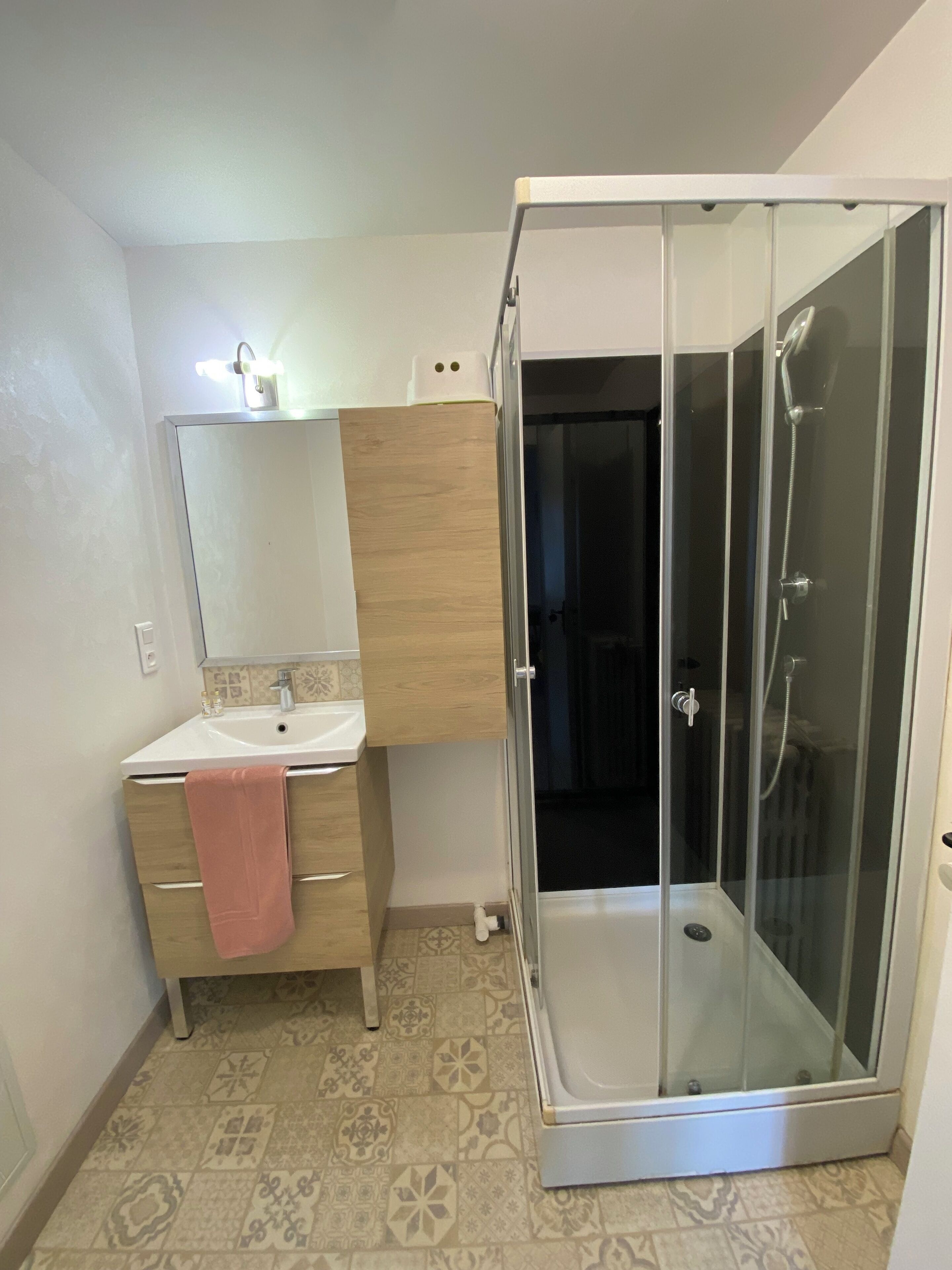 A bathroom with a sink, mirror, wooden cabinet, and a glass-enclosed shower.
