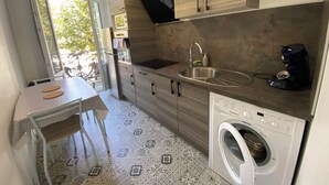 A compact kitchen with a sink, coffee maker, and washing machine. - Le repos des Thermes (Rochefort)