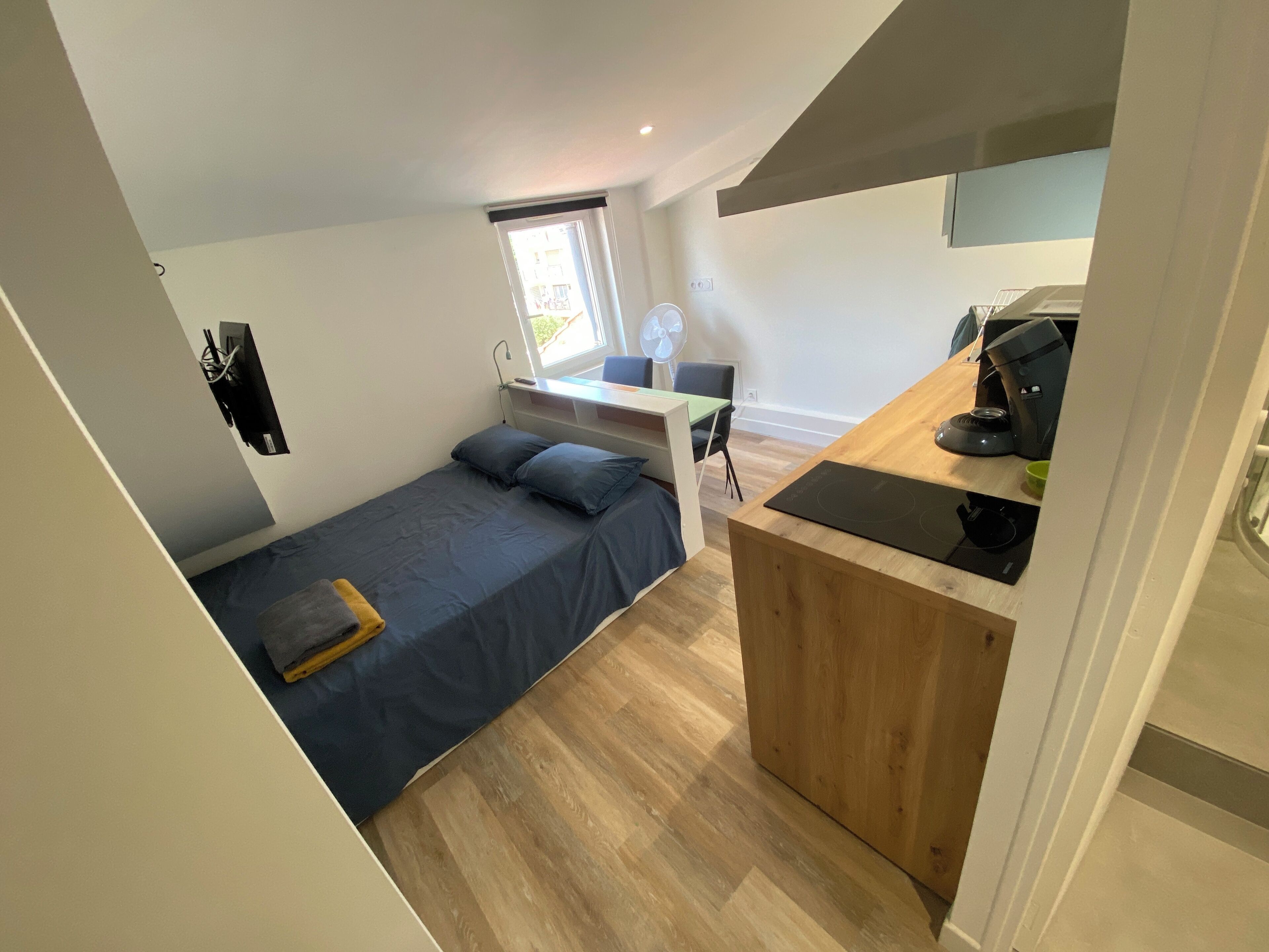 Een knus slaapkamer met een enkel bed, een klein bureau en een kitchenette.