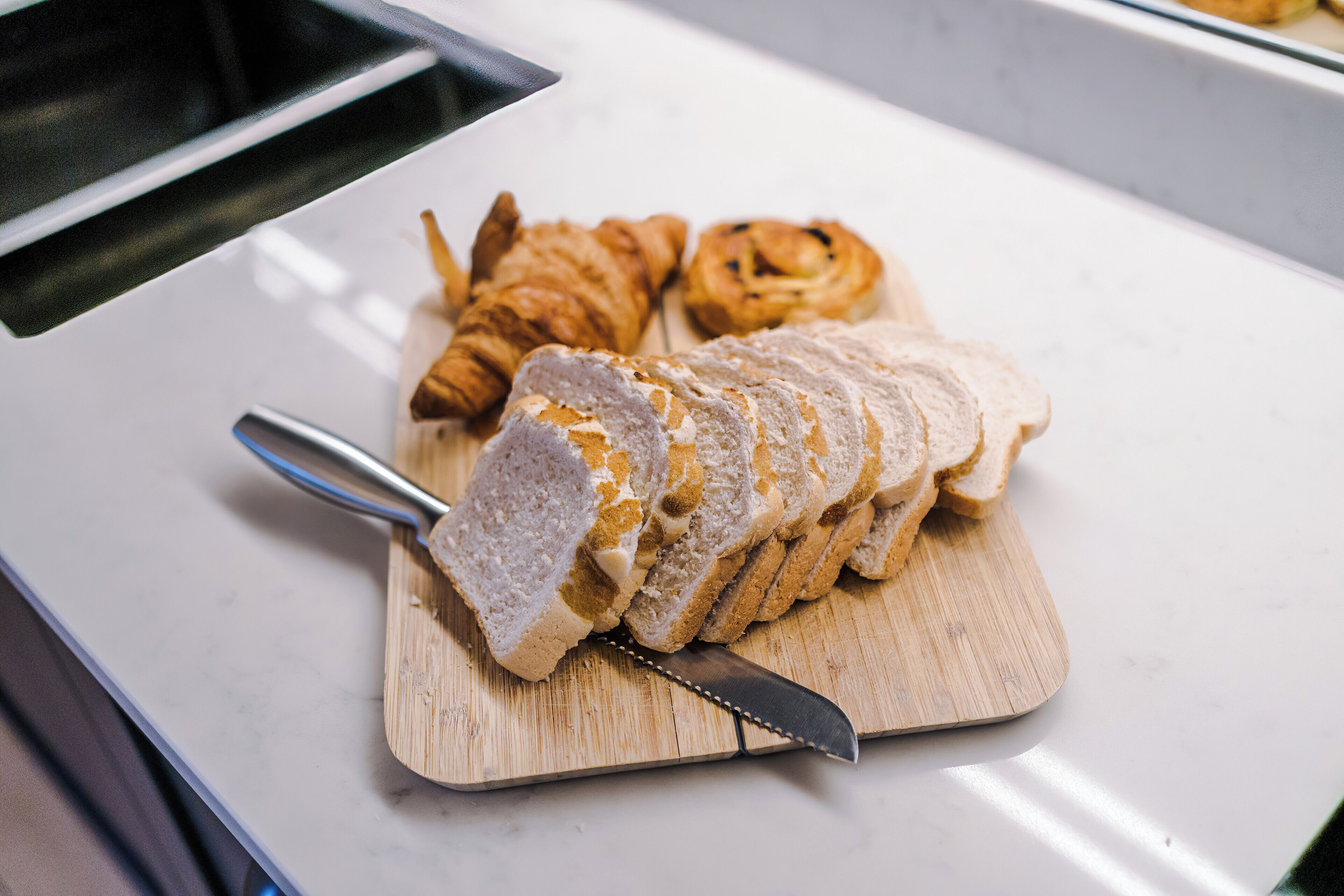 Sliced bread and croissants on a wooden cutting board.