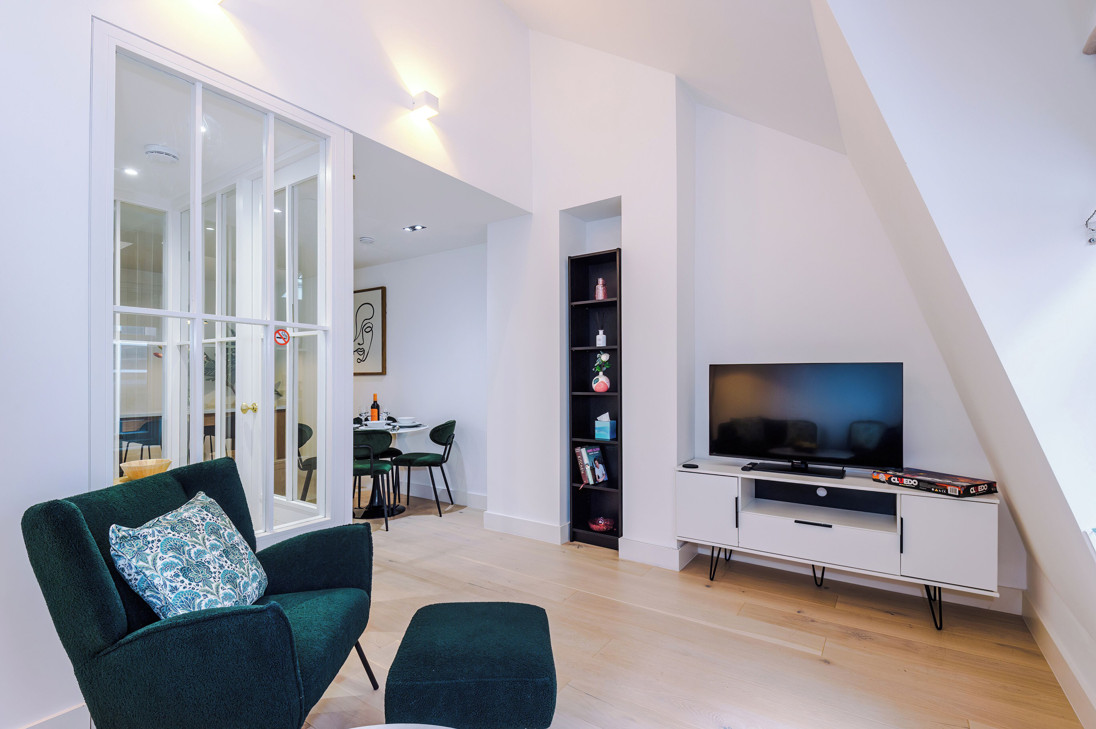 A modern living room with a green armchair, a flat-screen TV on a white stand, and a dining area in the background.