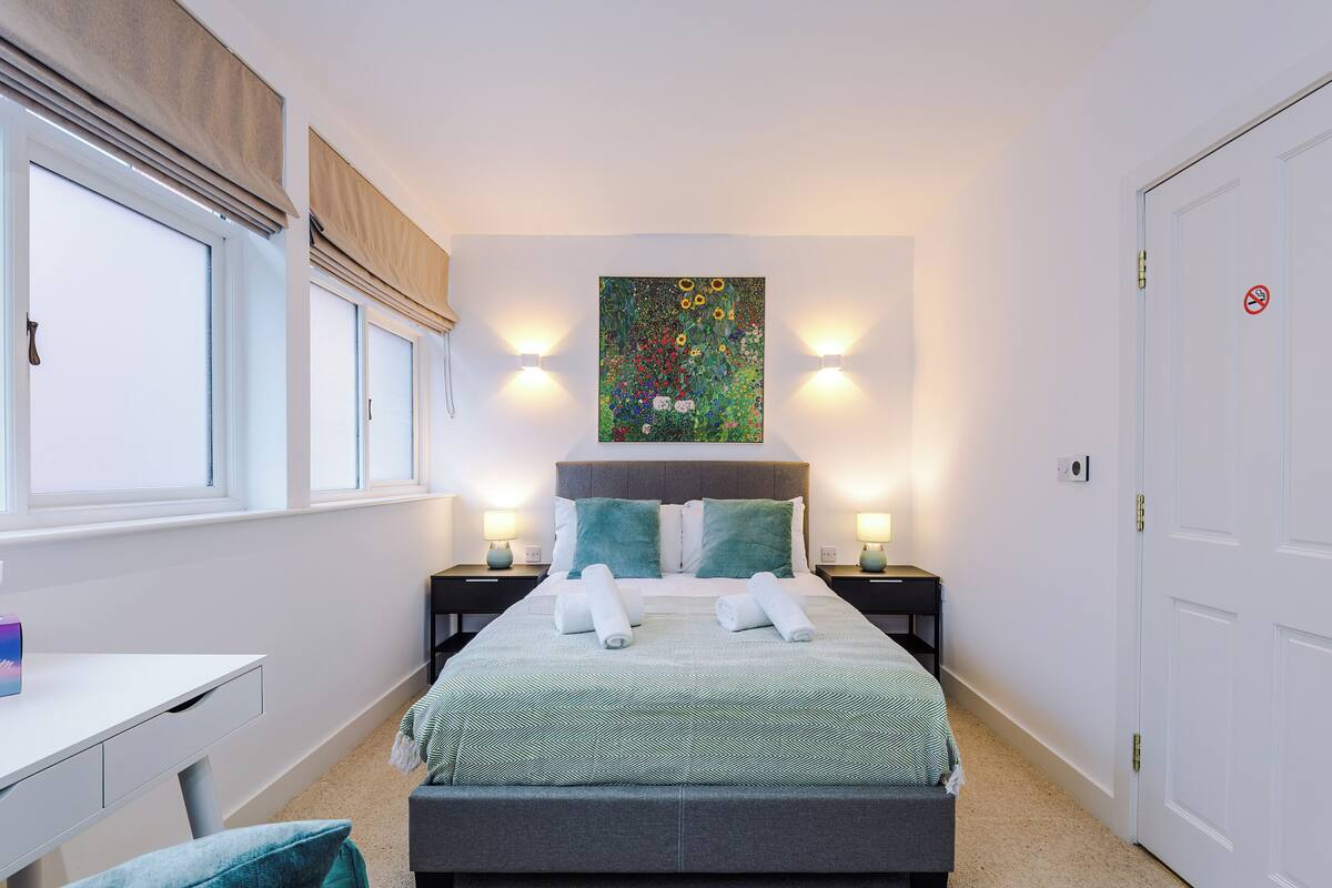 Ein ordentlich eingerichtetes Schlafzimmer mit einem Bett, Nachttischen, einem Schreibtisch und einem Fenster.