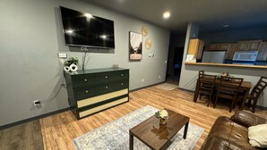 A living room with a TV, wooden flooring, a dark green dresser, a coffee table, and a brown leather sofa. - Modern 2-bed with full kitchen, in-unit laundry, and off-street parking. Near downtown Fairbanks. (Fairbanks)