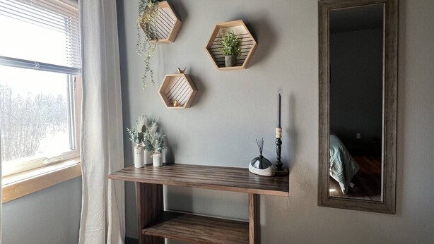 A room with a wooden desk, hexagonal shelves with plants, a mirror, and a window with curtains. - Modern 2-bed with full kitchen, in-unit laundry, and off-street parking. Near downtown Fairbanks. (Fairbanks)