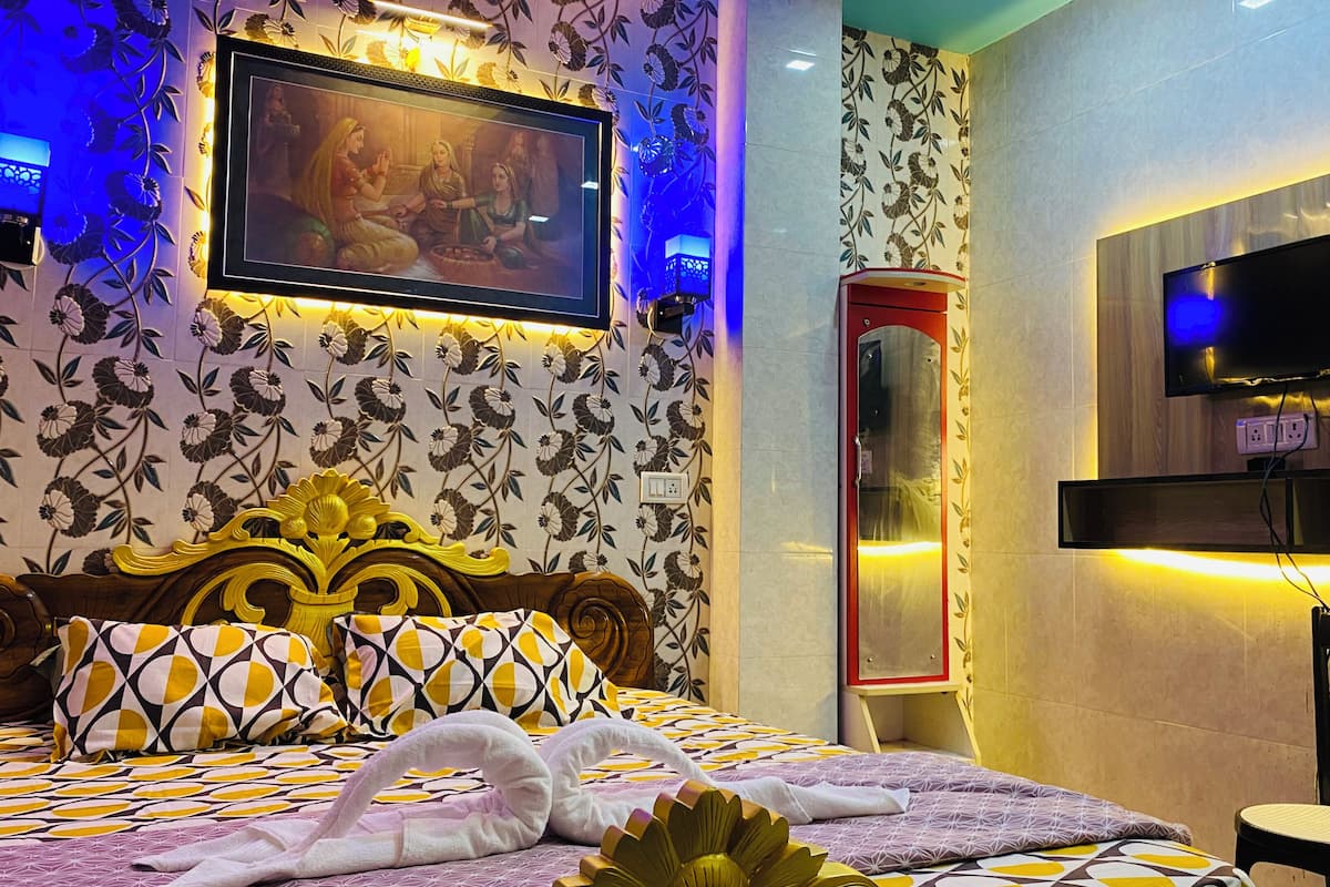 A hotel room with a bed, a television, a wall-mounted TV, and a floral-patterned wallpaper.