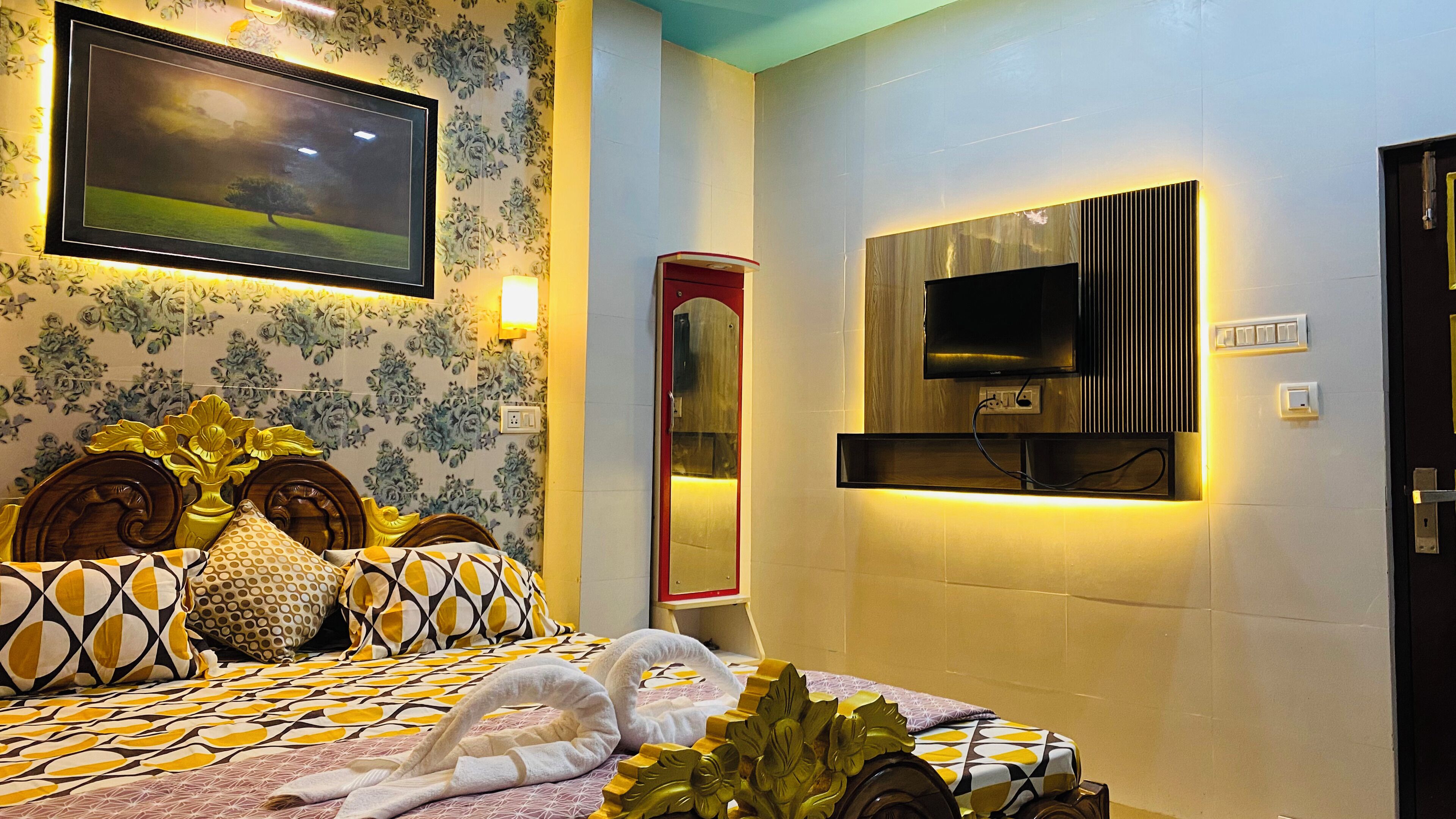 A hotel room with a bed, a TV mounted on the wall, and a floral wallpaper design.