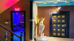 Una zona de bar con un letrero de neón, una estatua de ángel y una puerta con un diseño geométrico.