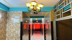 Un pasillo con paredes de piedra, un candelabro y cortinas rojas.